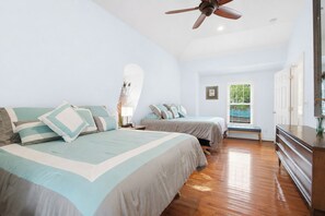 A bedroom with two beds, a ceiling fan, a bedside table with a lamp, and a window with blinds.