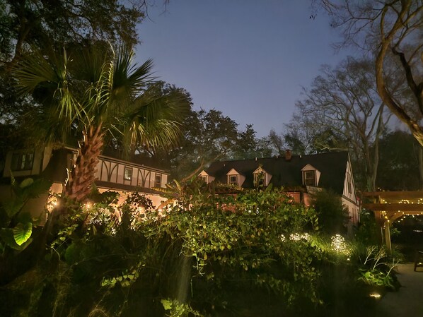Ein traditionelles Gebäude mit mehreren Giebeln, umgeben von üppigem Grün und beleuchtet mit Lichterketten.
