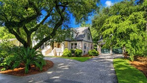 A residential house with a driveway, front yard, and surrounding trees. - Serene Cottage with Lush Landscaped Grounds (Charleston)
