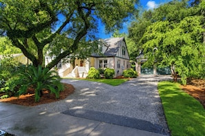 A residential house with a driveway, front yard, and surrounding trees. - Serene Cottage with Lush Landscaped Grounds (Charleston)
