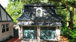 A two-story house with a steeply pitched roof, a small circular window on the upper level, and a garage with two doors. - Serene Cottage with Lush Landscaped Grounds (Charleston)