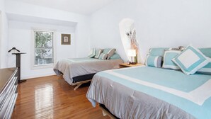 A bedroom with two beds, a ceiling fan, a bedside table with a lamp, and a window with blinds. - Serene Cottage with Lush Landscaped Grounds (Charleston)
