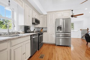 A modern kitchen with white cabinetry, stainless steel appliances, and a wooden floor. - Serene Cottage with Lush Landscaped Grounds (Charleston)