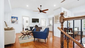 A spacious living room with a ceiling fan, a dining area with a wooden staircase, and a kitchen in the background. - Serene Cottage with Lush Landscaped Grounds (Charleston)