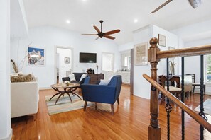 A spacious living room with a ceiling fan, a dining area with a wooden staircase, and a kitchen in the background. - Serene Cottage with Lush Landscaped Grounds (Charleston)