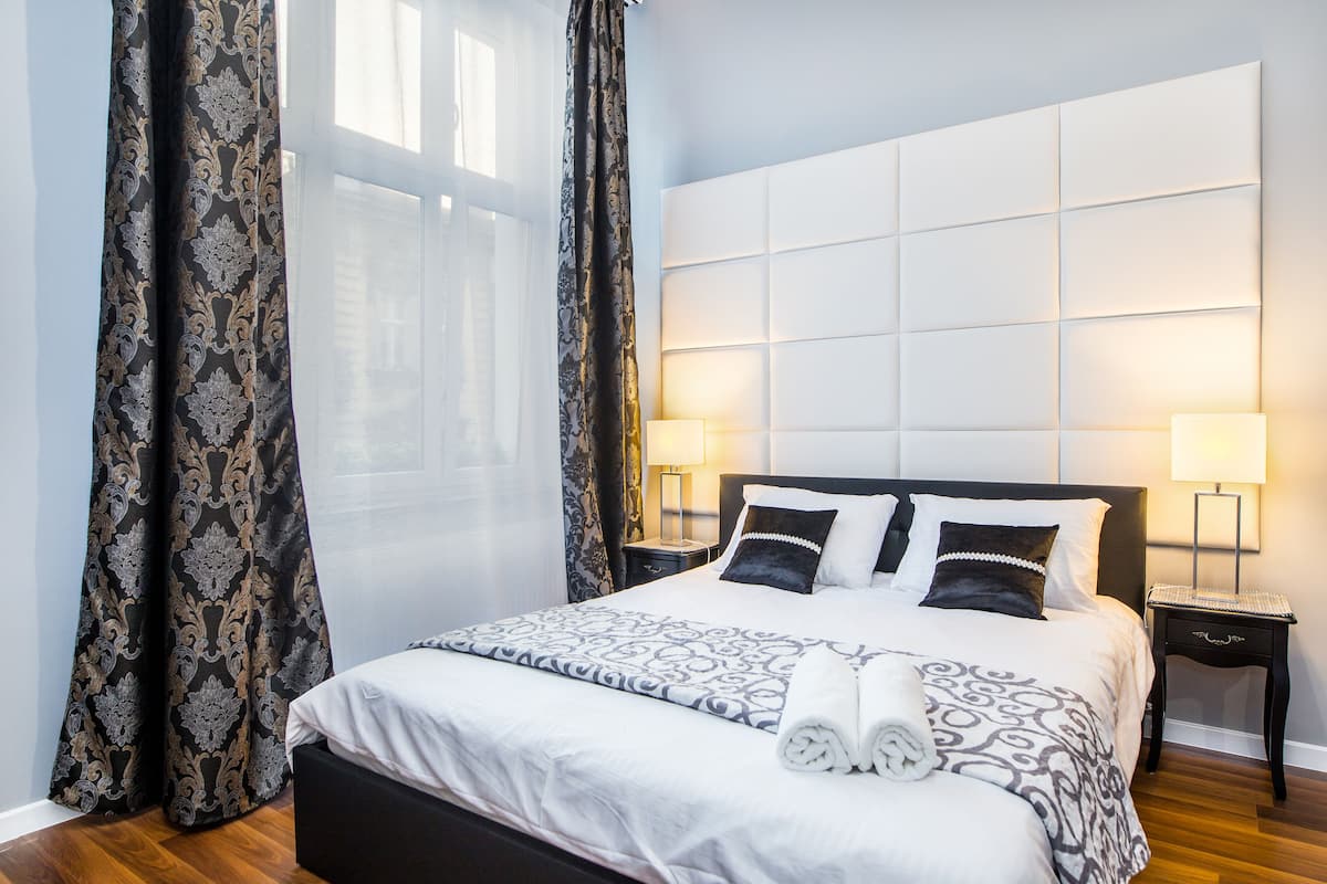 A neatly made bed with a patterned bedspread, two bedside lamps, and a headboard with a light panel.