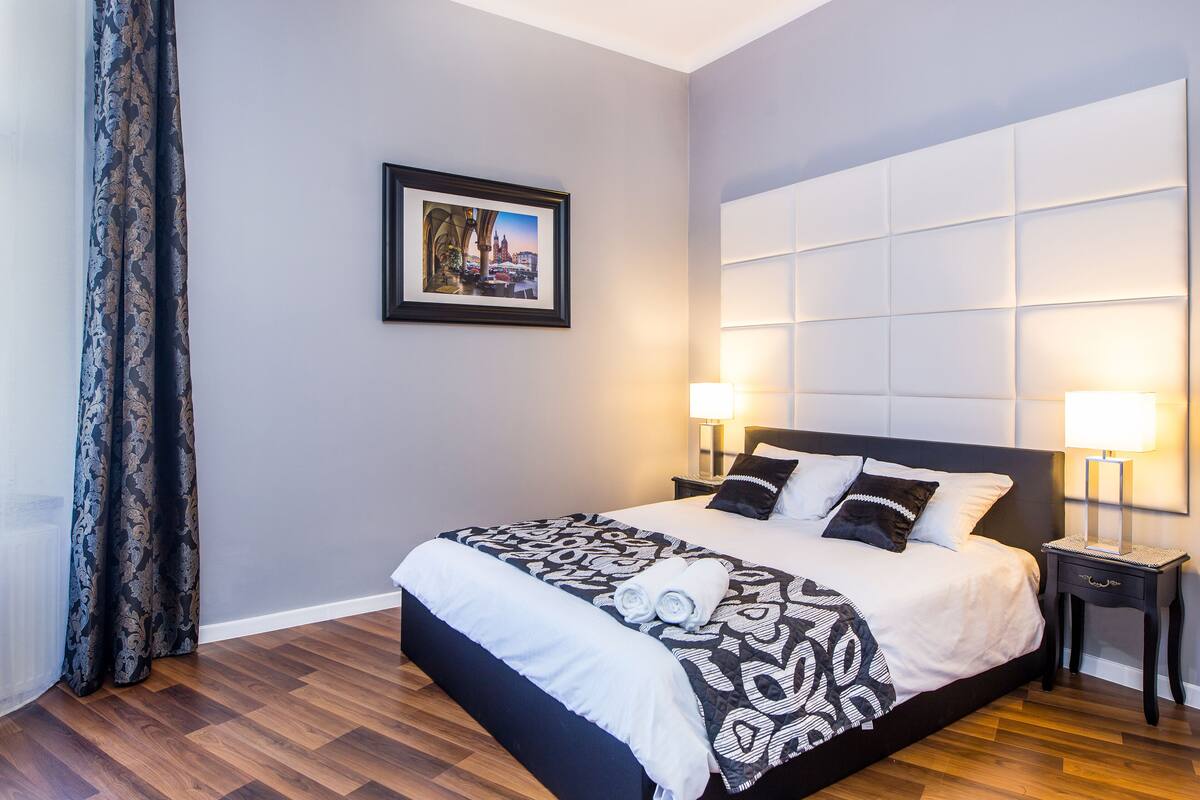 A modern hotel room with a large bed, two bedside tables, a framed picture on the wall, and a patterned bedspread.