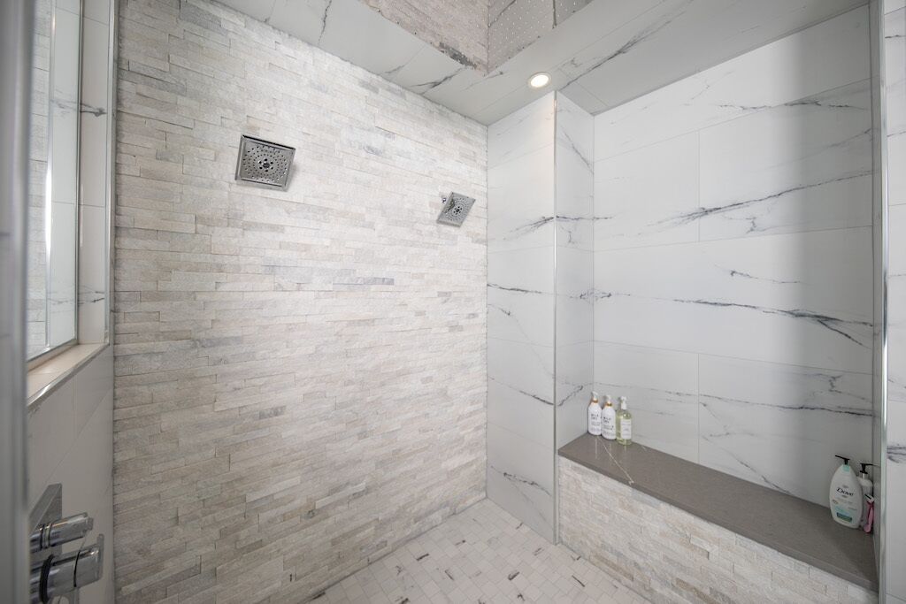 A modern bathroom with a marble shower wall, a built-in shelf with toiletries, and a visible drain.