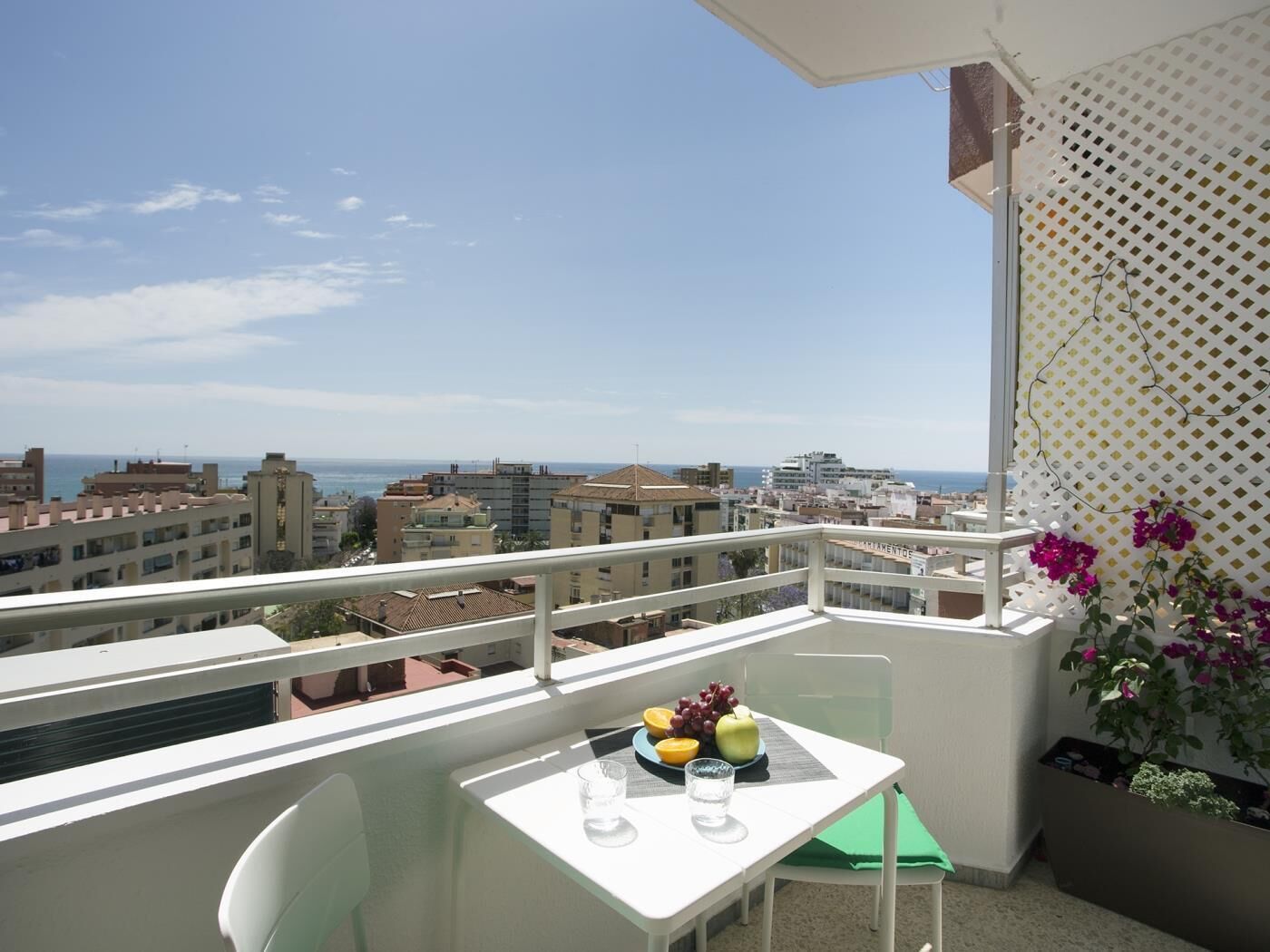 A balcony with a table set for two, overlooking a cityscape and the sea.