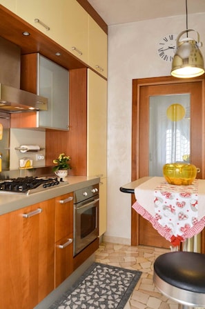 A compact kitchen with wooden cabinets, a gas stove, an oven, and a small table with a checkered tablecloth.