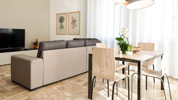 A modern living room with a sofa, dining table, chairs, a TV, and artwork on the wall.