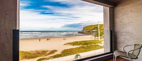 Una stanza con un'ampia finestra vista spiaggia, con pavimento in legno e una sedia in vimini.