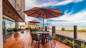 A wooden deck with outdoor seating and umbrellas, overlooking a beach. - Baluarte Pousada (Torres)