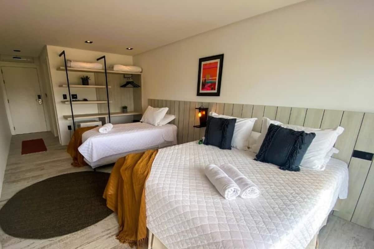 A hotel room with two beds, a wardrobe, a desk, and a small seating area.