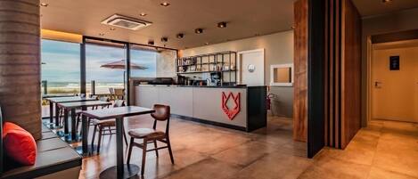 A modern hotel lobby with a bar area, seating, and a view of the beach.