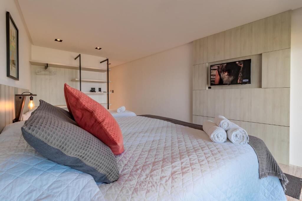 Una habitación de hotel moderna con una cama grande, un televisor de pantalla plana en la pared y toallas ordenadas sobre la cama.