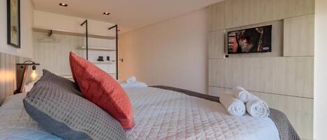 Una habitación de hotel moderna con una cama grande, un televisor de pantalla plana en la pared y toallas ordenadas sobre la cama.