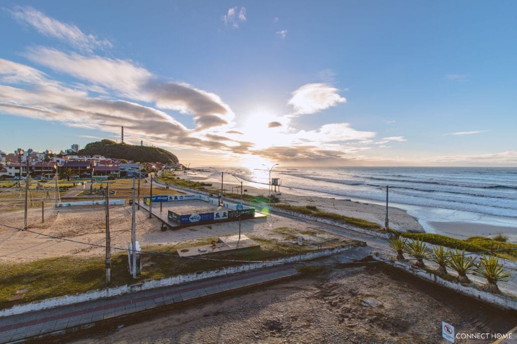 A coastal area with a beach, a train track, and a small building with a sign.