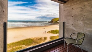 A room with a large window overlooking a beach, a chair, and a concrete wall. - Baluarte Pousada (Torres)