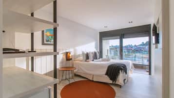 Un dormitorio moderno con una cama grande, una mesita pequeña y vistas a la ciudad a través de un ventanal amplio.