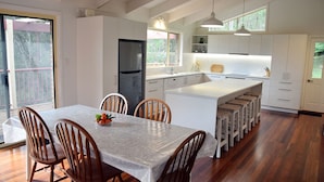 A modern kitchen with a central island, wooden chairs, and a dining table. - Arakoon Heights - close to South West Rocks - Bring your own linen (Arakoon)