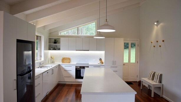 A modern kitchen with white cabinetry, a central island, a built-in oven, and a large window providing natural light. - Arakoon Heights - close to South West Rocks - Bring your own linen (Arakoon)