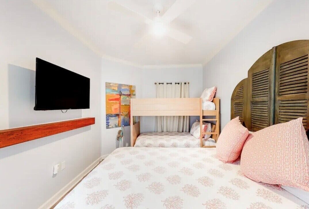 A bedroom with a bunk bed, a flat-screen TV mounted on the wall, and a ceiling fan.