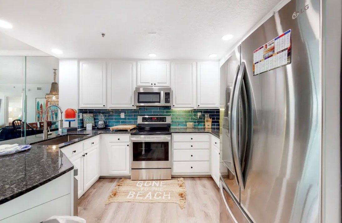 A modern kitchen with white cabinets, a stainless steel refrigerator, a microwave, and a built-in oven.
