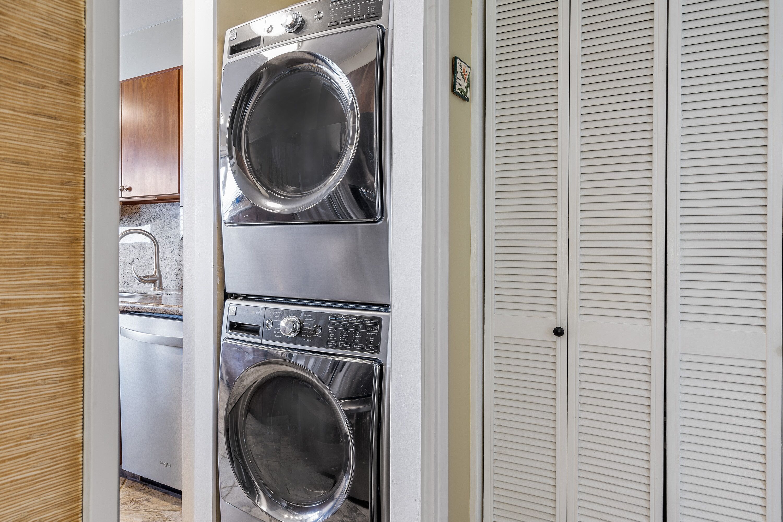 A laundry area with two stacked front-loading washing machines and a closed white louvered closet.