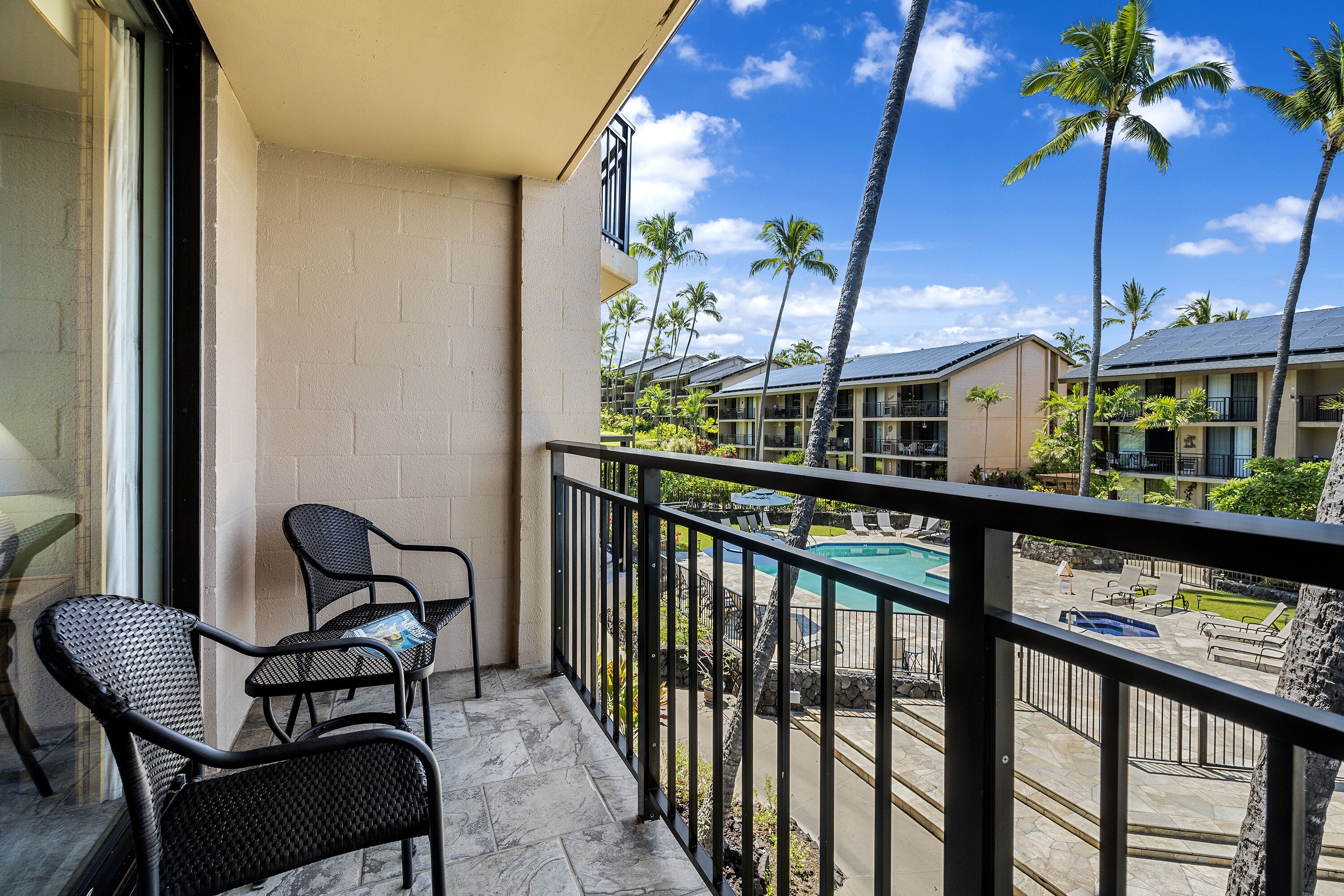 Ein Balkon mit zwei Korbstühlen, einem Pool und Palmen im Hintergrund.