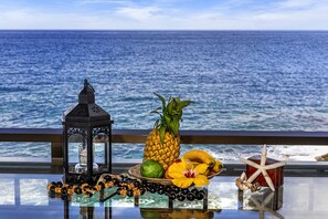 Une table avec une lanterne, un ananas, une banane, un citron vert et une étoile de mer, placée près d’une rambarde d’où l’on peut admirer l’océan.