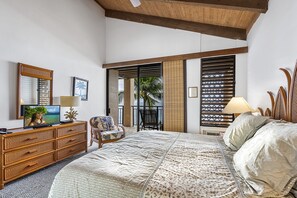 Une chambre avec un grand lit, une commode en bois, une chaise, un téléviseur et un balcon donnant sur des palmiers.
