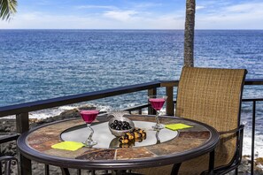 Une table ronde sur laquelle sont disposés un verre contenant une boisson rose, un bol d’olives et un verre à martini, le tout placé sur un balcon offrant une vue sur l’océan.