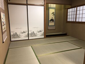 Una habitación japonesa tradicional con suelo de tatami, puertas correderas con obras de arte y un celosía de papel shoji.