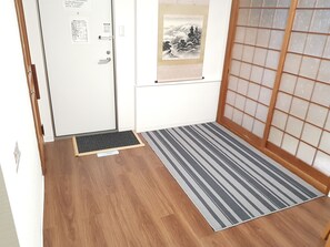 Habitación de hotel con piso de madera, un tapete a rayas, un divisor japonés y una puerta con lector de tarjeta.