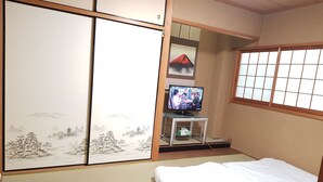 A traditional Japanese room with tatami flooring, a sliding shoji screen, a television on a low table, and a futon bed. - Osaka Namba House (Osaka)