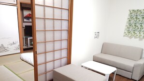 A room with a sliding shoji screen, a beige sofa, a small white table, and a tatami mat. - Osaka Namba House (Osaka)