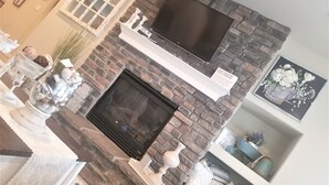 Une cheminée surmontée d’un téléviseur, entourée d’objets décoratifs et d’un panneau indiquant la disponibilité du Wi-Fi.