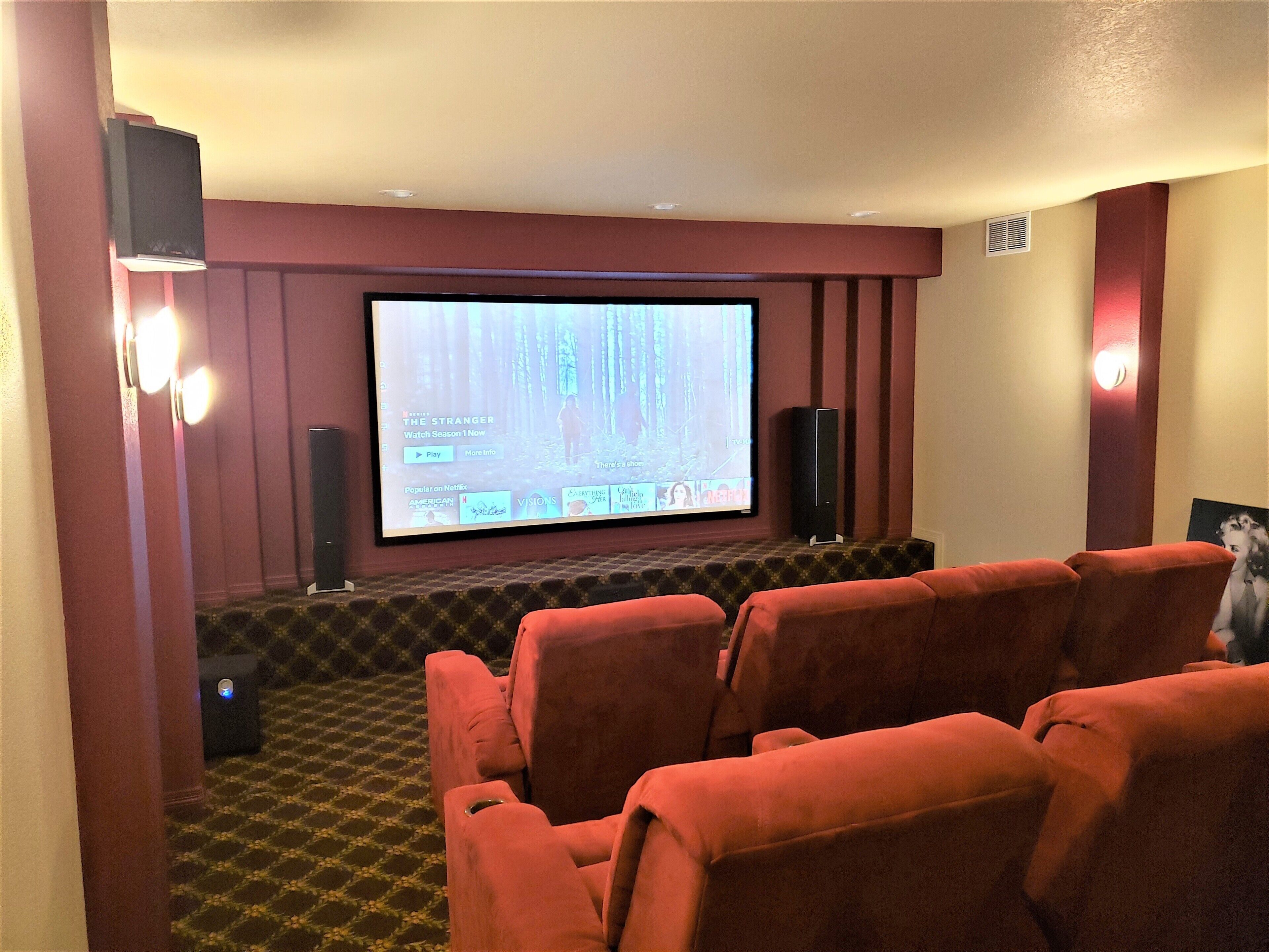 A home theater with a large screen, red seating, and a carpeted floor.