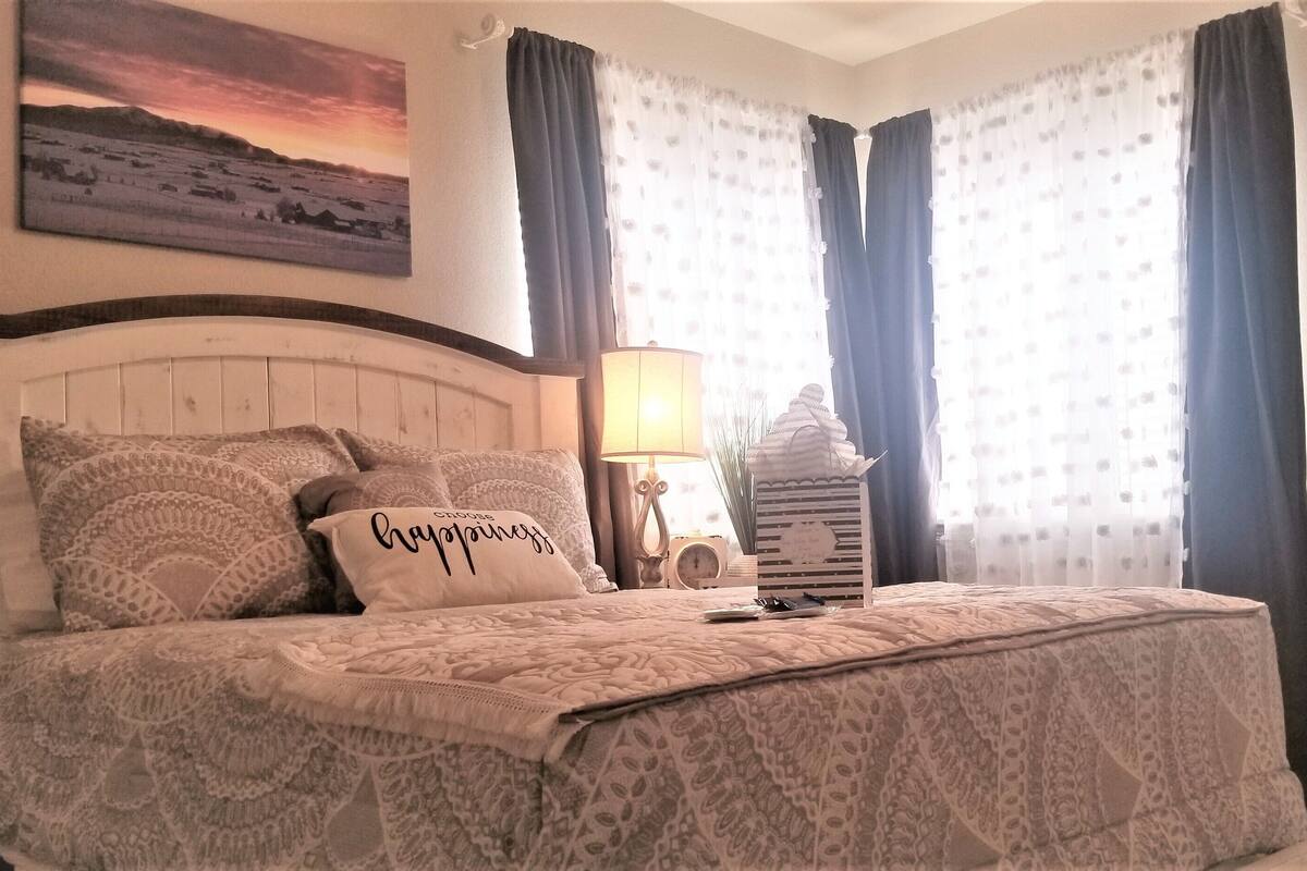 A neatly made bed with a patterned bedspread and pillows, a bedside lamp, and a framed picture on the wall.