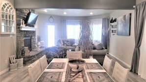 Un coin repas avec une table dressée pour quatre personnes, une cheminée, un téléviseur et une vue sur le salon.