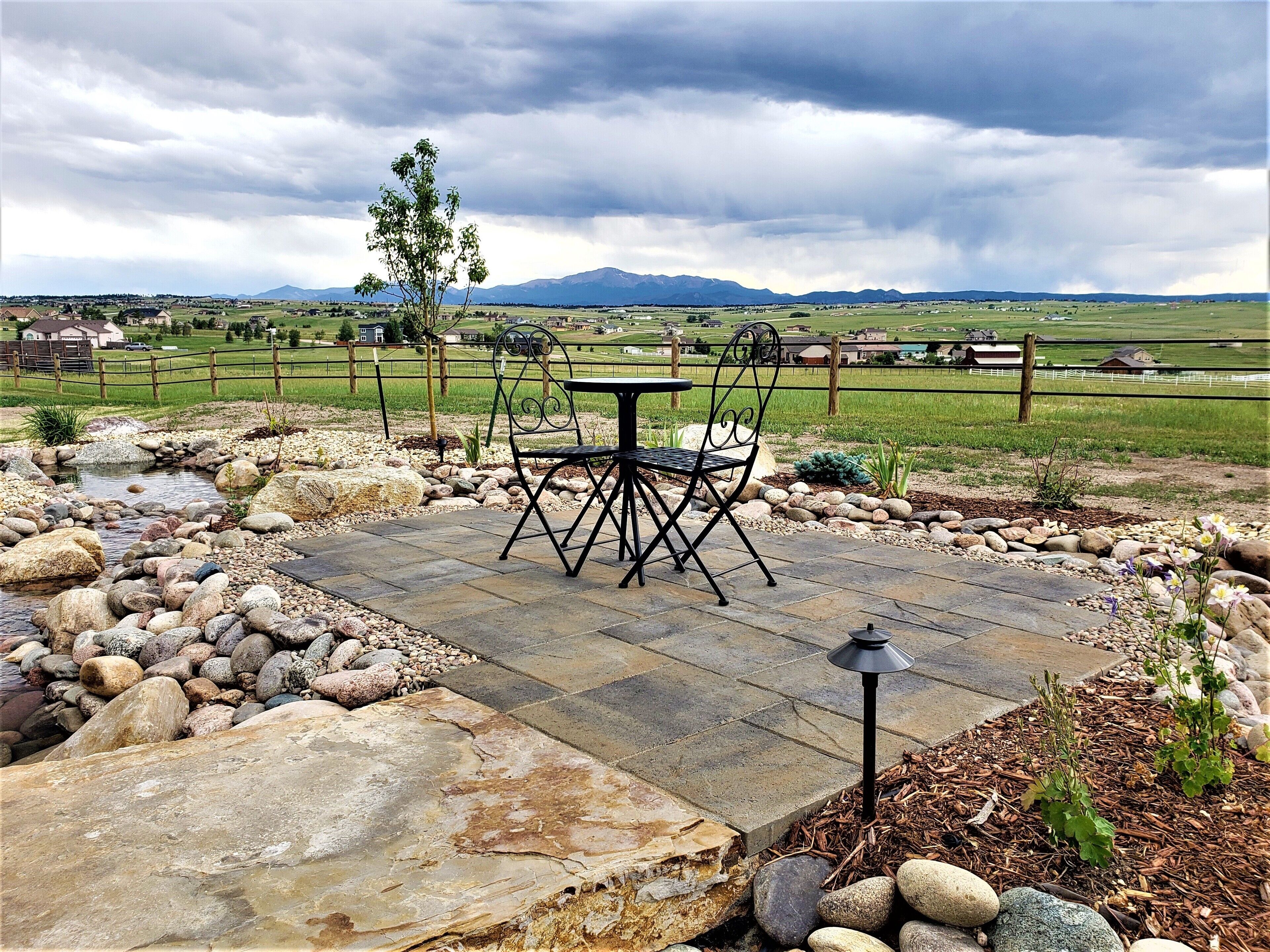 Une terrasse extérieure avec une table et des chaises en pierre, entourée de rochers et d’un petit ruisseau.