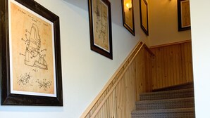 A staircase with wooden handrails and carpeted steps, leading to a landing with framed patent drawings on the wall. - Schweitzer Ski Condo, Sandpoint, Lake Pend Oreille (Sandpoint)