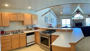 A kitchen with wooden cabinets, a dishwasher, a stove, and a built-in oven. There is a large island with a sink and a stone fireplace. - Schweitzer Ski Condo, Sandpoint, Lake Pend Oreille (Sandpoint)