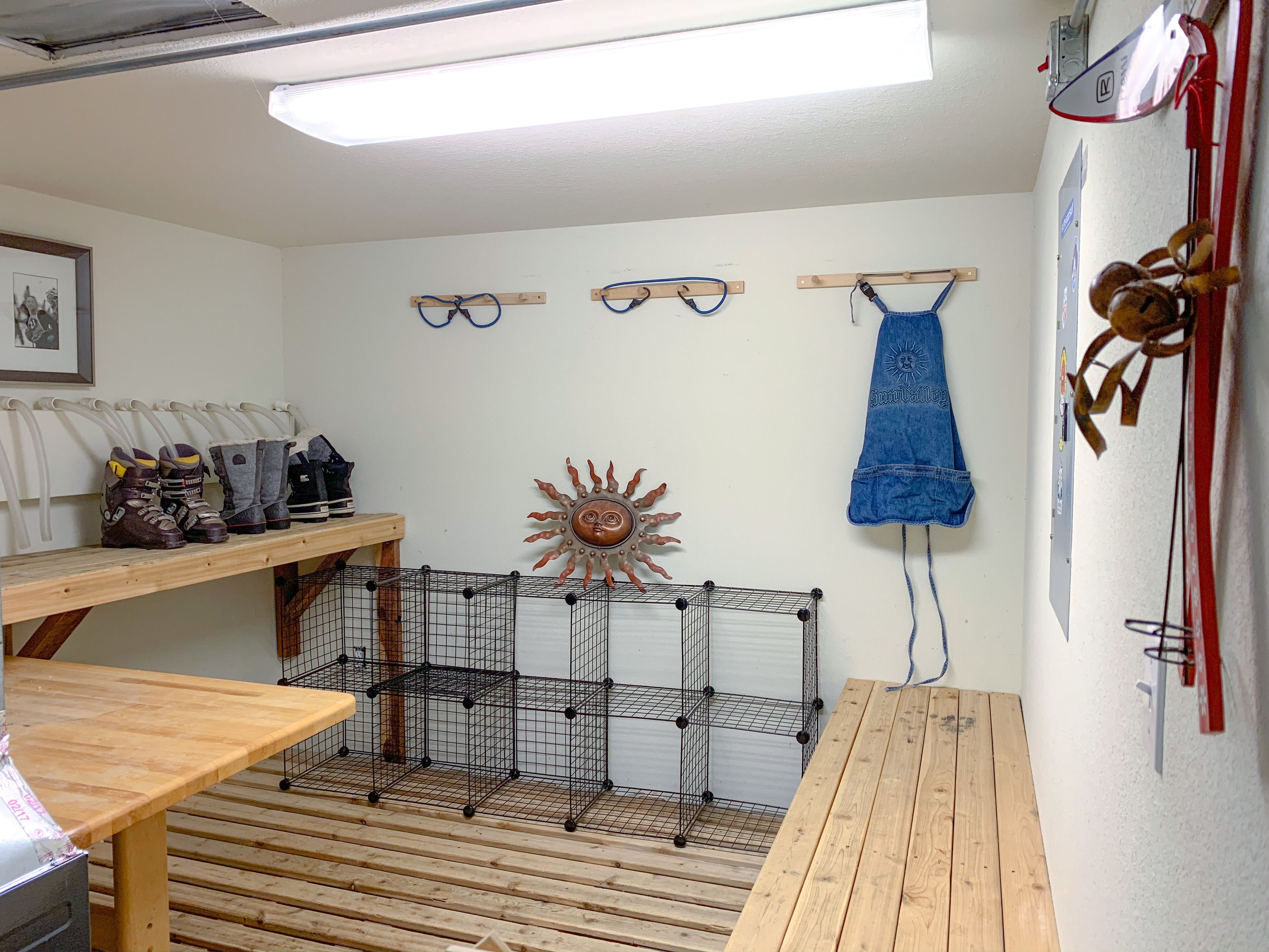 A room with a wooden table, a wire cage, a wooden bench, and a wall-mounted rack with shoes.