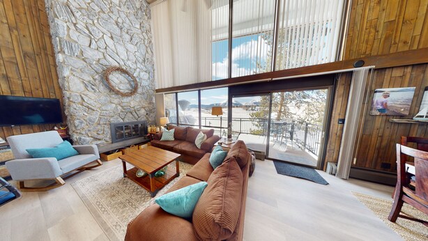 A spacious living area with a stone wall, large windows, and a cozy seating arrangement. - On Lake, WOW Views! 4 Kings, Big Deck. Walk to Marina, Concerts, Events (Dillon)