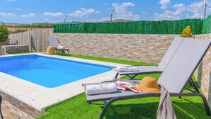 Une piscine avec des chaises longues et une haie verdoyante.