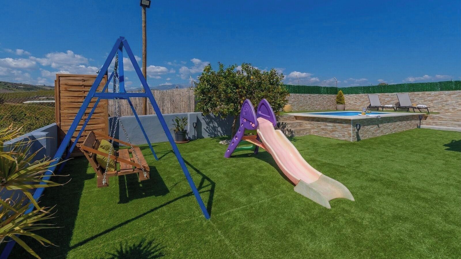 A playground with a swing set and a slide, surrounded by a well-maintained lawn and a pool area.