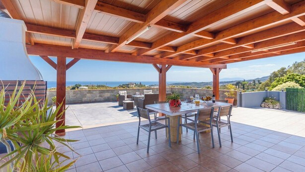 Une terrasse couverte avec une table et des chaises, un barbecue et une vue sur la mer.