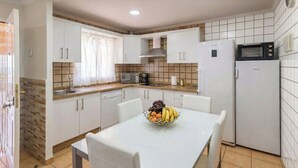 Une cuisine compacte avec des meubles blancs, un four à micro-ondes, un réfrigérateur et une table à manger agrémentée d’un panier de fruits.